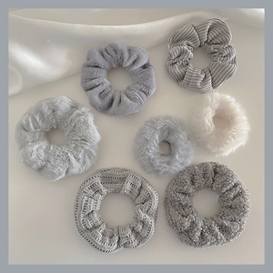 Flat lay of seven plush scrunchies in grey tones with diverse textures on white silk