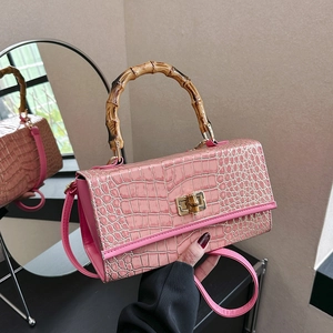 Detail of pink croc-embossed handbag featuring a unique bamboo handle and gold twist lock