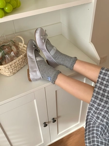 Detail of silver-purple satin ballet flats with bow and grey lace socks on wooden floor