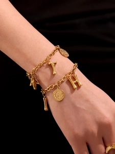 Macro detail of 18k gold-plated chain bracelet with Elizabeth coin and letter pendants