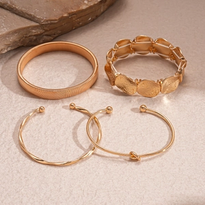 Detail of four-piece gold geometric bracelet set on a textured stone background