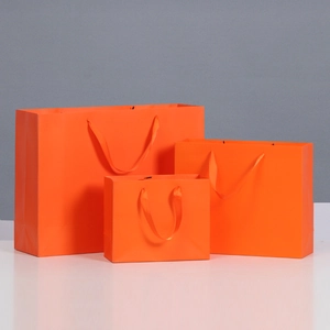 Three vibrant orange gift bags in various sizes with elegant matching silk handles
