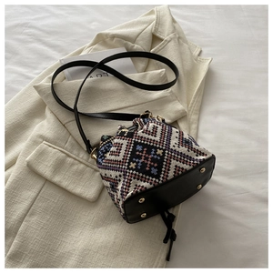 Detail of woven bucket bag featuring geometric jacquard fabric and black leather base