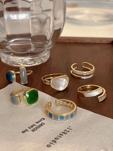 Collection of gold rings with emerald stones and pearls on a dark wooden tray