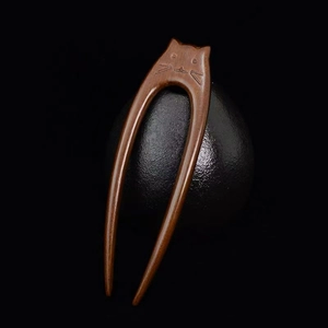 Macro shot of creative cat-shaped dark sandalwood hair pin on a textured black sphere