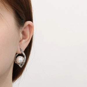 Close-up of silver irregular hammered hoop earring with white pearl on model's ear