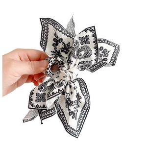 Elegant black and white paisley bow hair clip in soft fabric held by hand on white backdrop