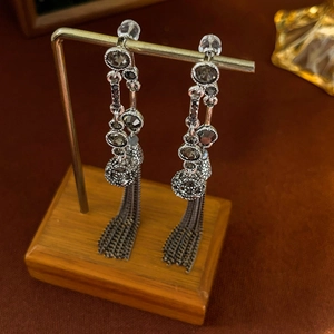 Detail of silver long tassel earrings with dark rhinestones on a wooden display stand