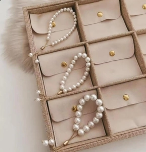 Adjustable pearl bracelets in three sizes with gold beads on a beige jewelry display tray