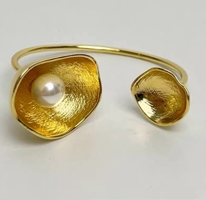 Makroaufnahme einer goldfarbenen Manschette mit Struktur und einer weißen Perle