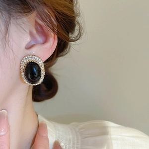Close-up of vintage oval gold earrings with black stone and pavé crystal halo