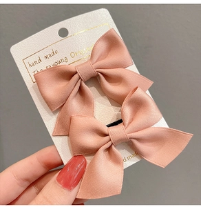 Detail of two pink satin bow hair clips on display card with soft silk luster texture