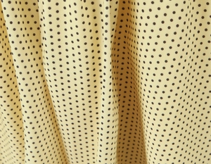 Détail du tissu jaune clair à pois noirs montrant la texture fluide et le drapé chic