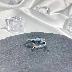 Detailed view of silver snake-shaped ring with blue gemstone on black stone background