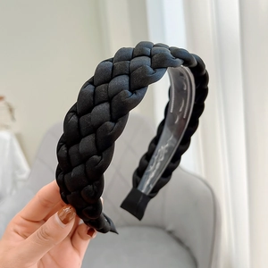 Close-up of a hand holding a black braided fabric headband with a clear plastic tooth grip