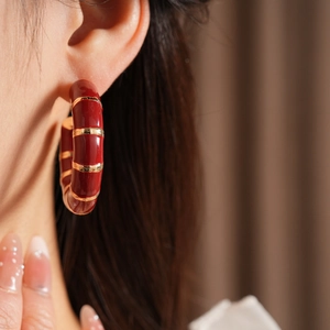 Close-up of red enamel C-shape earring with gold stripes worn by a model