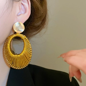 Détail de boucles d'oreilles créoles ovales dorées avec texture tressée métallique
