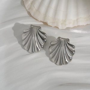 Macro shot of silver scallop shell stud earrings on white silk with natural seashell