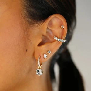 Close-up of gold plated silver earrings set featuring sparkling crystals on a model's ear