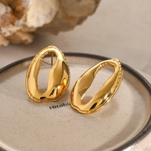 Macro detail of gold 18k irregular hollow earrings on a minimal ceramic tray