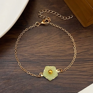Detail of a gold-plated bracelet featuring a delicate green flower pendant on wood