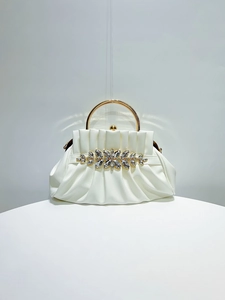 Detail of white pleated evening clutch featuring a gold metal handle and crystal flower cluster