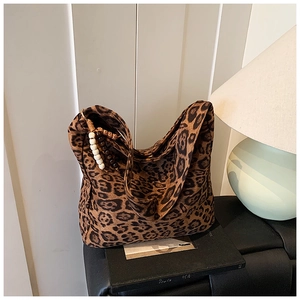Detail of leopard print tote bag with wooden bead charm on a leather chair background