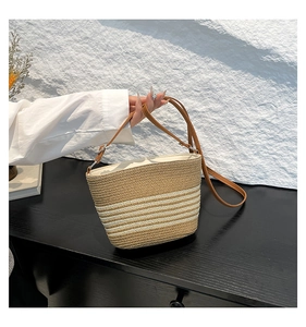 Detail of khaki straw bucket bag with white stripes and brown leather shoulder strap