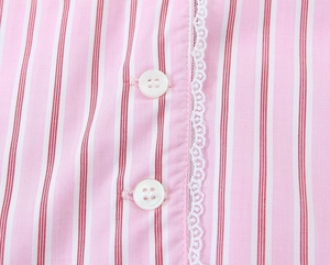 Gros plan sur tissu rayé rose avec bordure en dentelle et boutons blancs de chemise