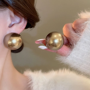 Gros plan de grandes boucles d'oreilles sphériques or champagne poli sur l'oreille
