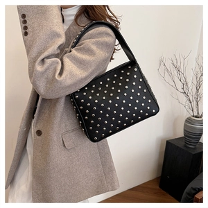 Street style view of a black punk rivet shoulder bag worn with a tailored grey blazer