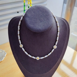 Detail of white heishi bead necklace with three daisy charms on a purple bust display