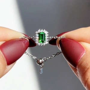 Macro shot of emerald cut green gemstone ring with adjustable silver chain and heart charm