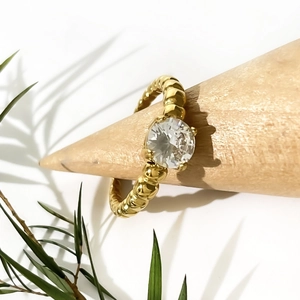 Elegant 18K gold ring with spiral texture and sparkling round zircon on wooden stand