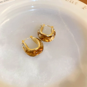 Macro shot of U-shaped amber resin earrings with golden metal borders on ceramic