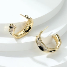 Detail of C-shaped golden earrings with leopard enamel patterns and white zircon stones