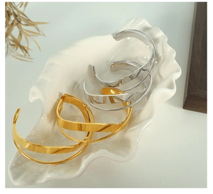 Close-up of minimalist gold and silver wide hoop earrings on a ceramic shell tray