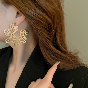 Macro detail of oversized gold hollow flower earring worn on a model in black suit
