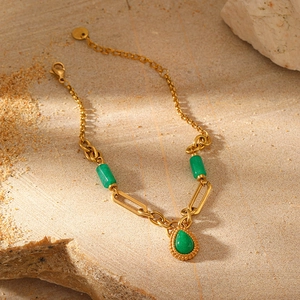 Detail of gold-plated bracelet with green stone teardrop pendant on natural rock background