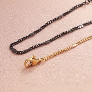 Minimalist black and gold Cuban link chains with secure lobster clasp on pink fabric