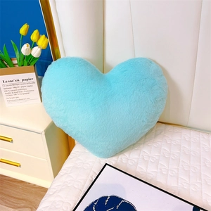 Gros plan d'un coussin en peluche bleu clair en forme de cœur sur un canapé blanc