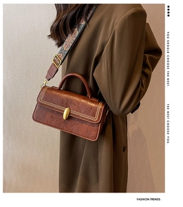 Detail of vintage brown leather bag with metallic rivets and geometric printed strap