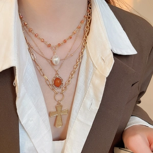 Close-up of layered necklace with pearl pendant, orange beads and a gold cross on a model
