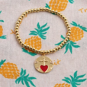 Gold beaded bracelet featuring a red heart and cross pendant on a pineapple pattern cloth