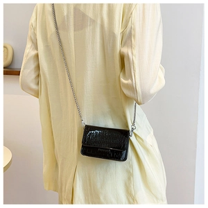 Detail of black crocodile texture bag with silver chain worn by a model in a suit