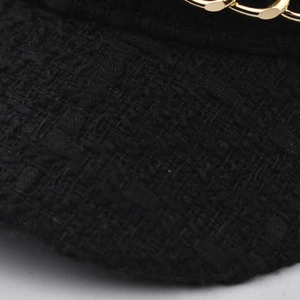 Close-up of black tweed newsboy cap featuring detailed golden chain metal decoration