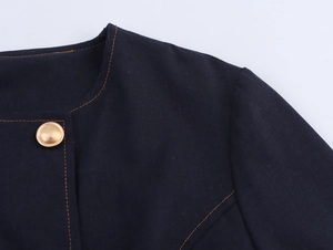 Detail of navy round neck top with orange contrast stitching and gold metal button