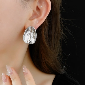 Close-up of irregular hammered silver metal earring worn on model ear