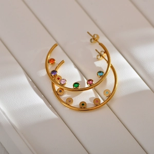 Detail of gold hoop earrings with multi-colored zircon stones on white texture