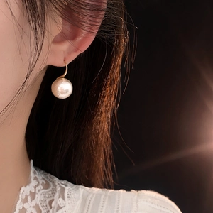 Détail d'une boucle d'oreille dorée avec perle blanche texturée sur le mannequin